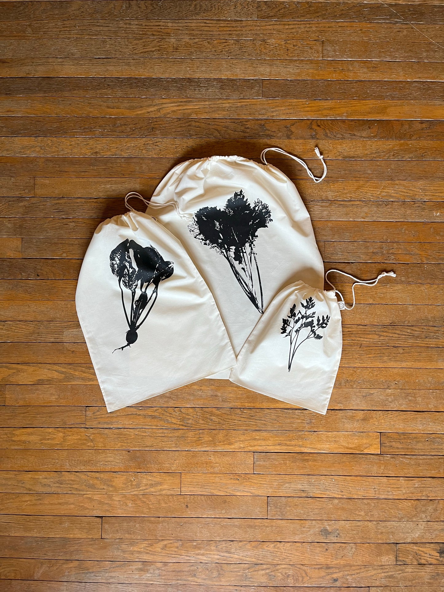 Three muslin, drawstring produce bags lie on a hardwood floor